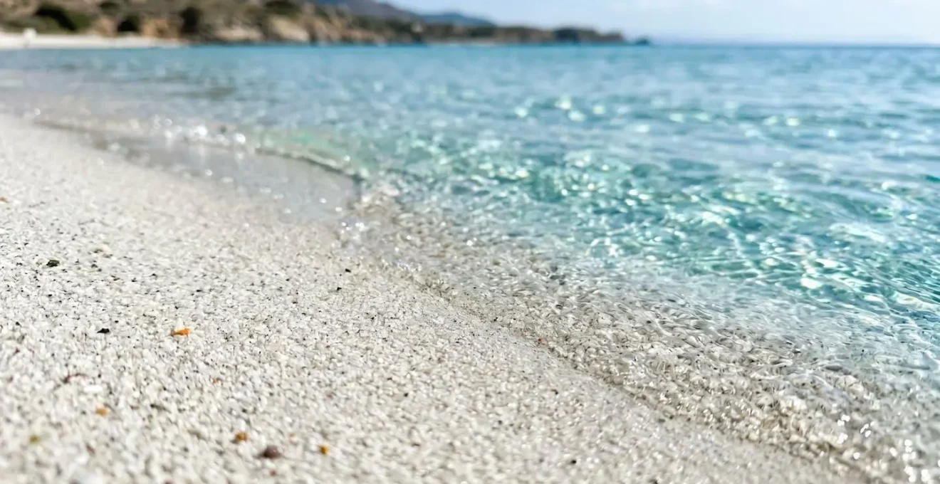 Gros plan sur le sable blanc fin rencontrant l'eau cristalline turquoise, texture détaillée d'une plage corse avec faible profondeur de champ