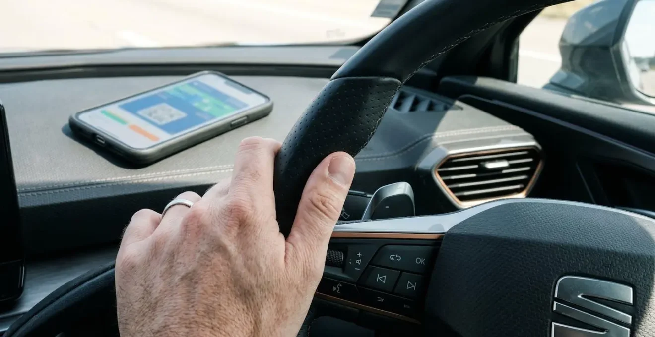 Gros plan d'une main posée sur un volant de voiture moderne avec smartphone affichant un e-ticket posé sur le tableau de bord, lumière naturelle latérale douce